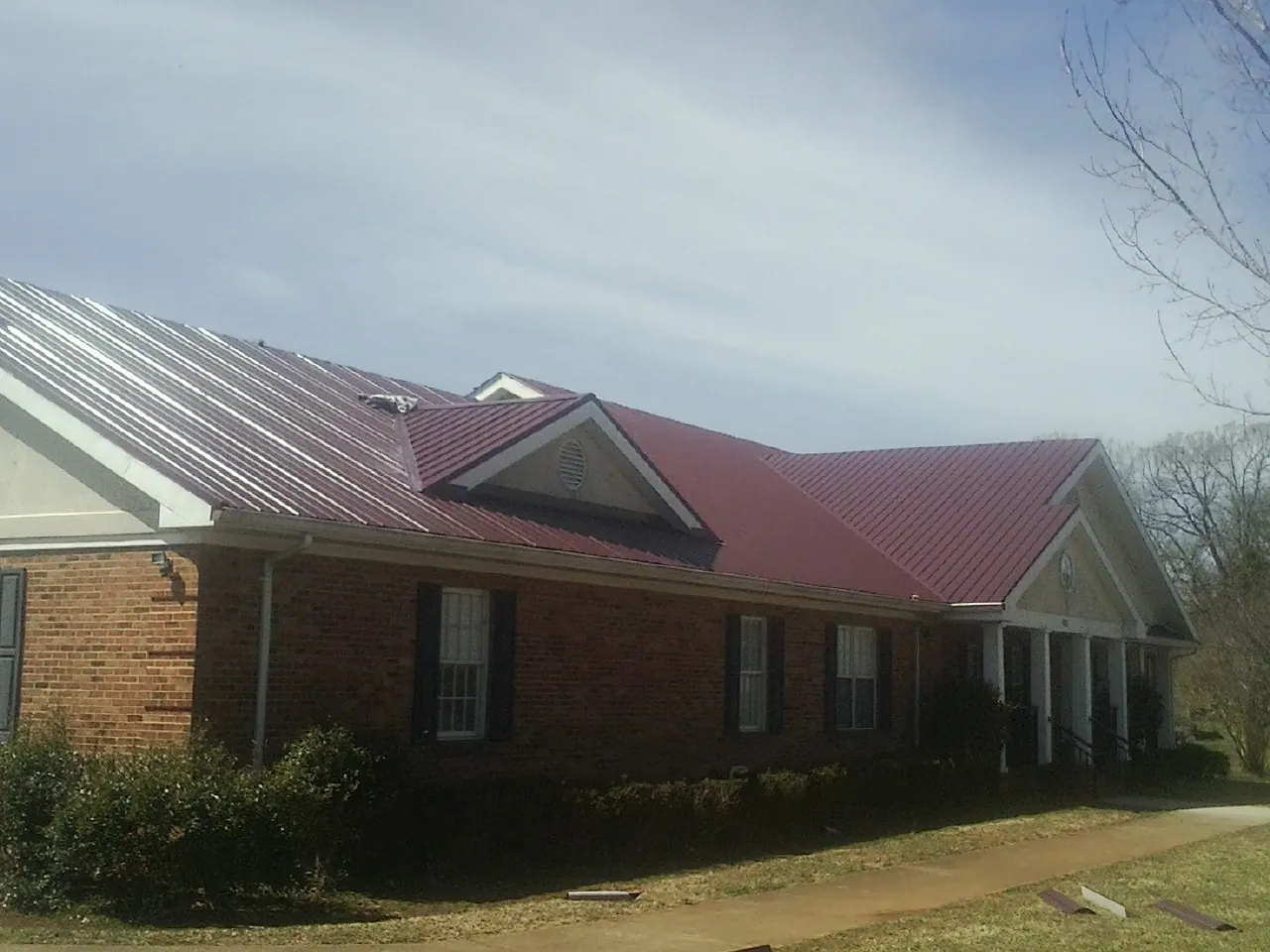 Red metal roof with gabled entries on a long brick building, from a Hail Damage Roof Repair job in Sicklerville
