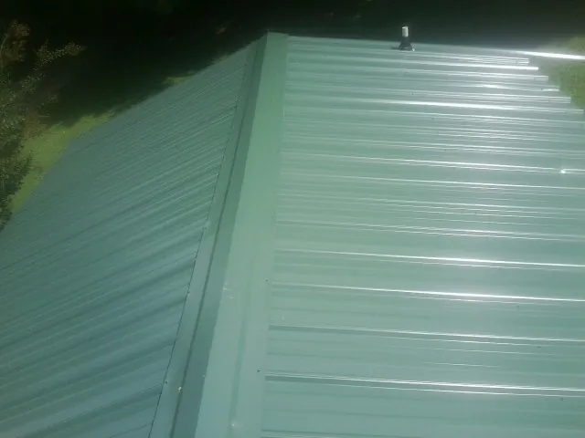 New green metal panels meeting at the ridge of a roof — Flat Roof Repair work by our crew in Sicklerville