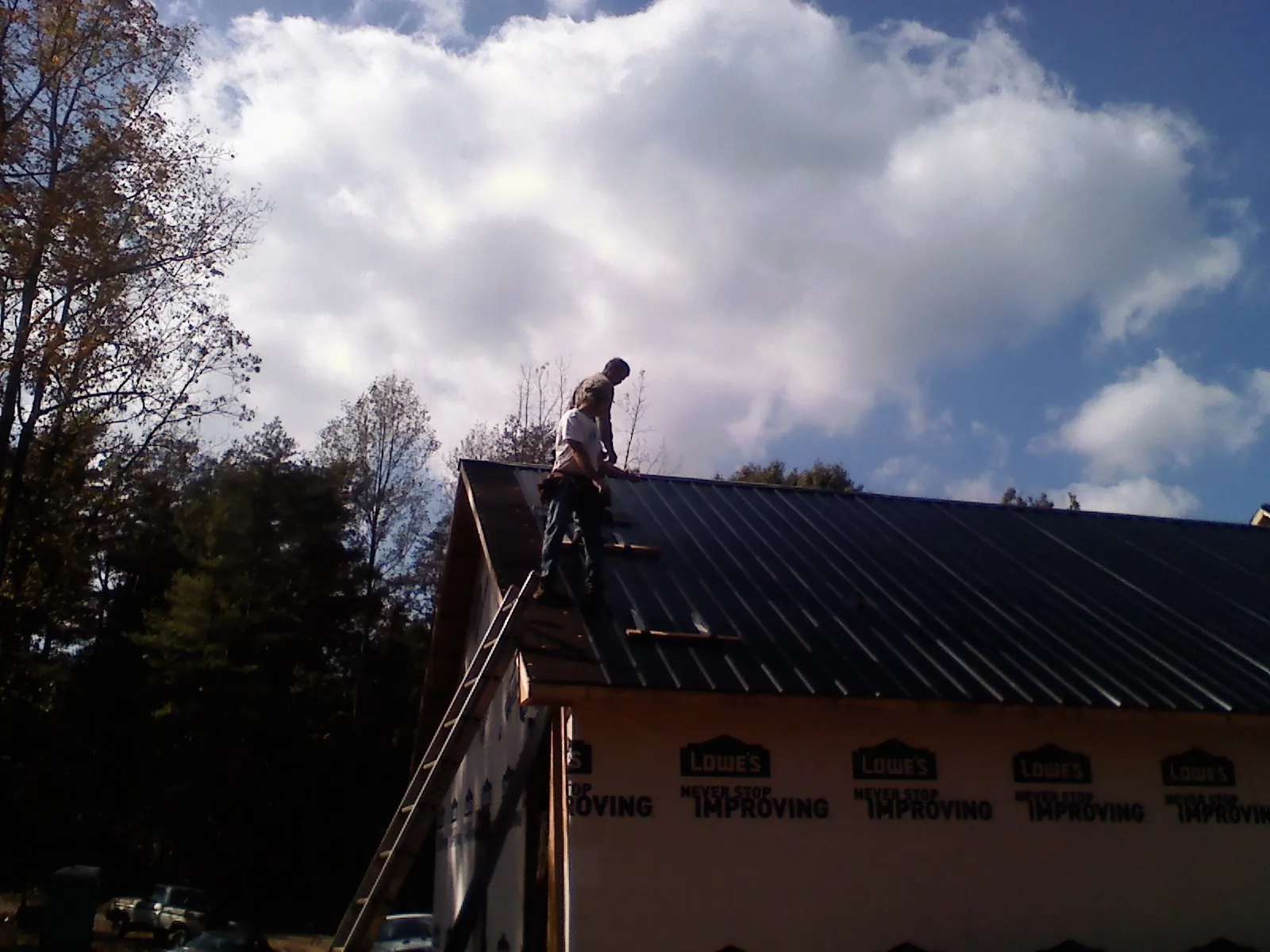 Roofer fastening dark metal panels high against a cloudy sky, from a Roof Inspection job in Sicklerville