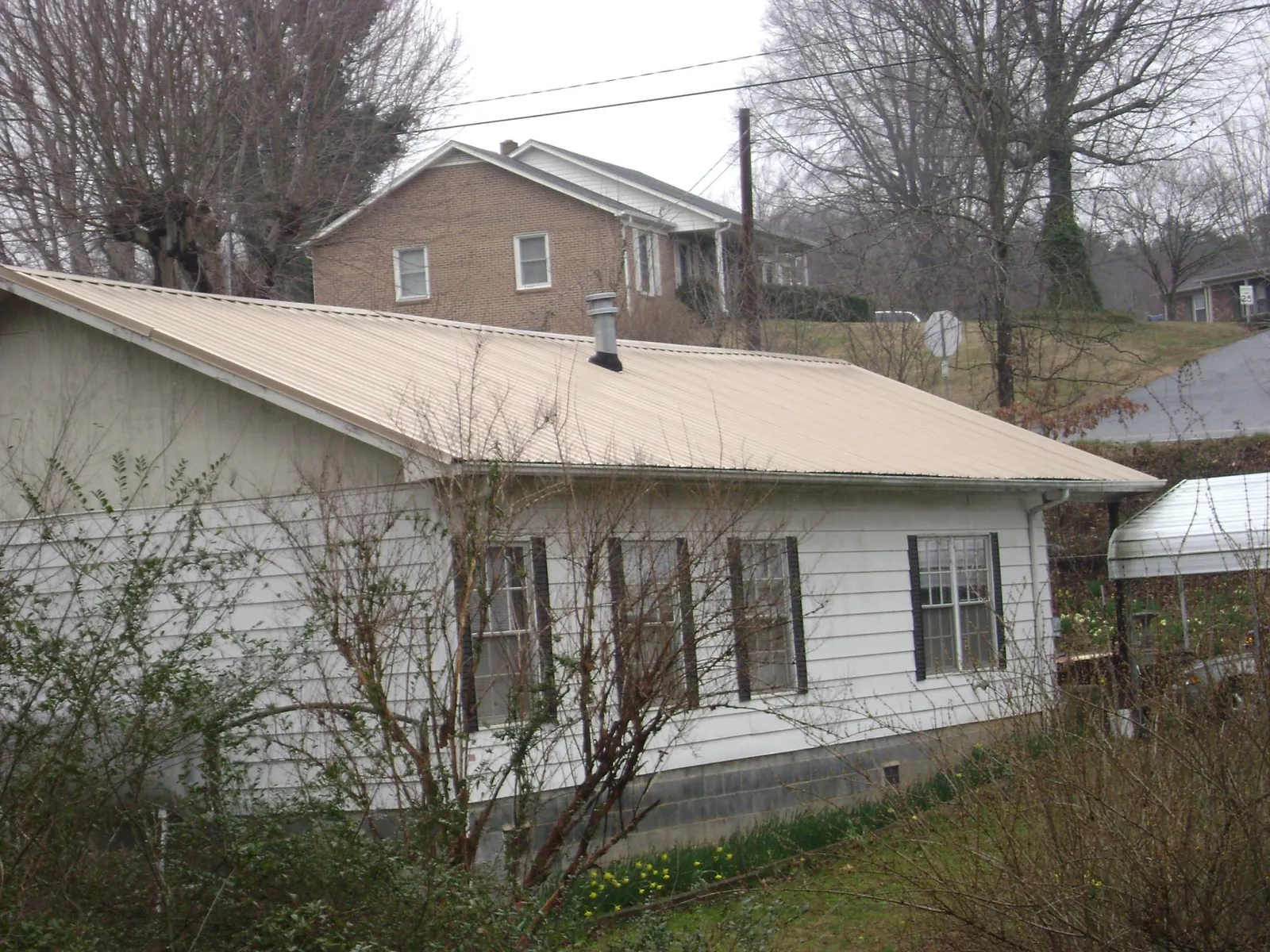 Tan metal roof on a white sided house set into a hillside — Commercial Roofing by Roofing Brothers in Sicklerville